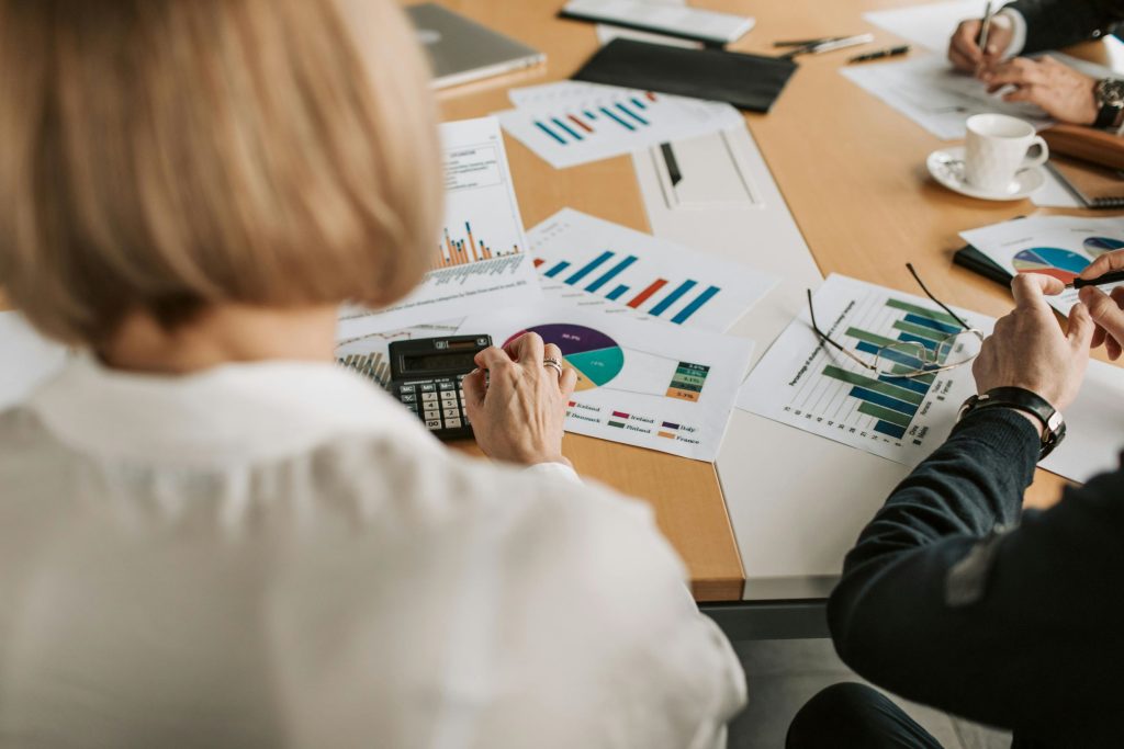 Reunião de equipe com gráficos e relatórios financeiros sobre a mesa, enquanto uma pessoa utiliza uma calculadora.